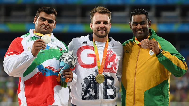 Three men who compete in shot put pose with their medals