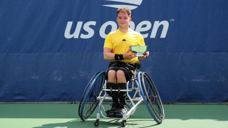 British male wheelchair tennis player smiles holding trophy