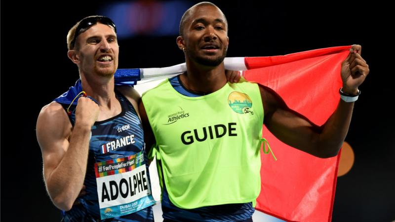 A white vision impaired man and his guide celebrate holding the French flag