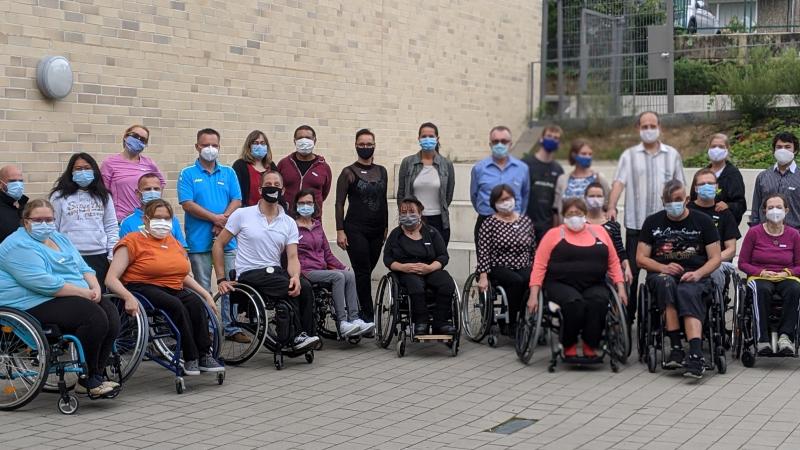 A group of wheelchair users outdoors with a group of standing people behind them