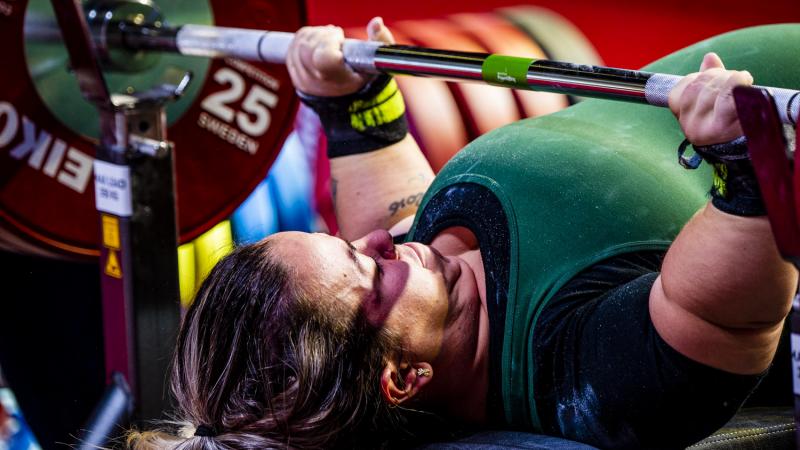 A short-stature woman lifting a bar on a bench press