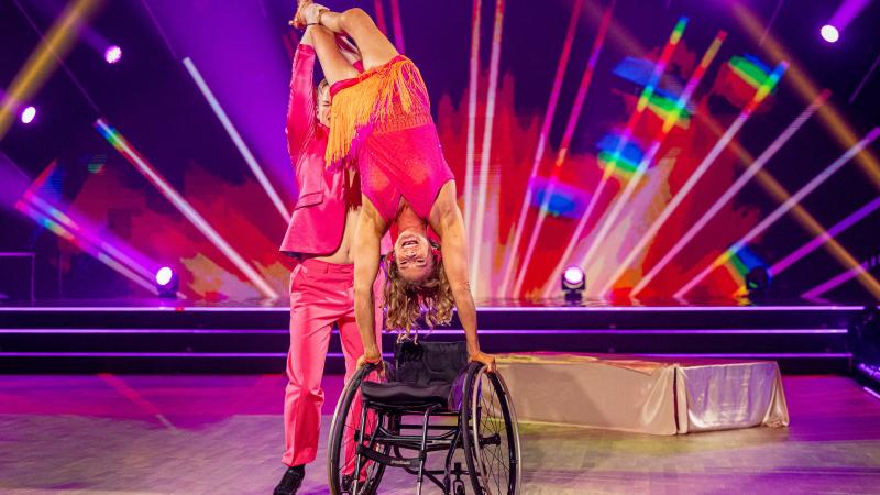 A woman in a wheelchair on a dance floor held by her dance partner