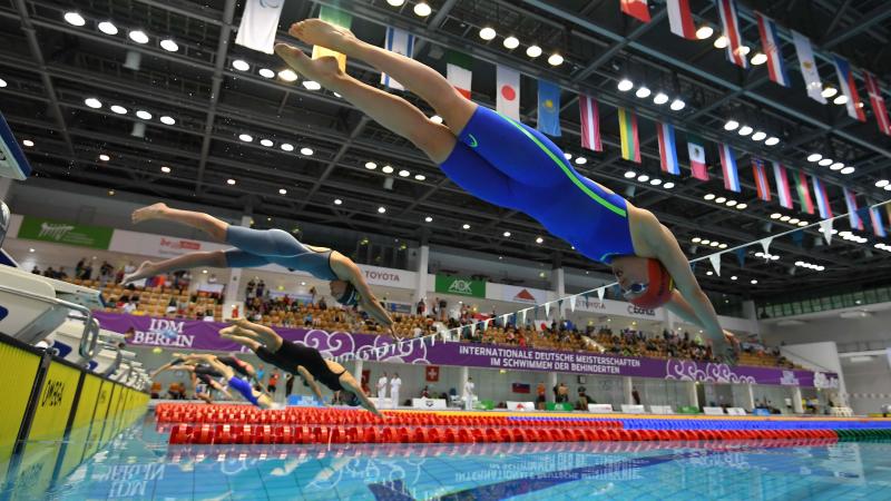 A group of seven female swimmers jumping in the water 