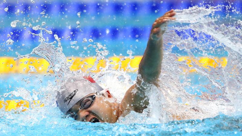 A man with a grey cap swimming in a pool