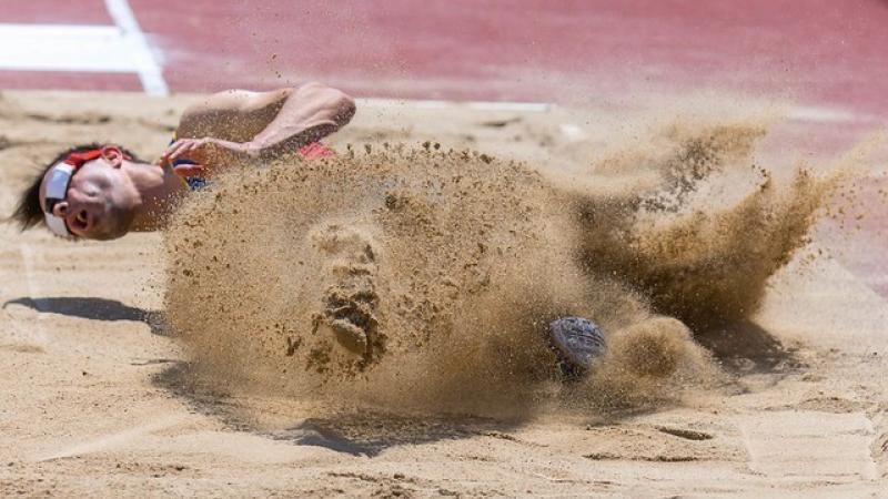 A man with a blindfold landing in a sand pit of a long jump track