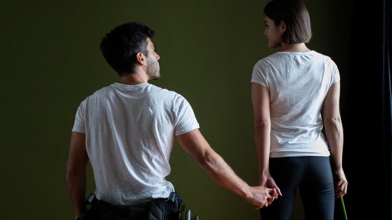 A man in a wheelchair holding the hand of a standing woman