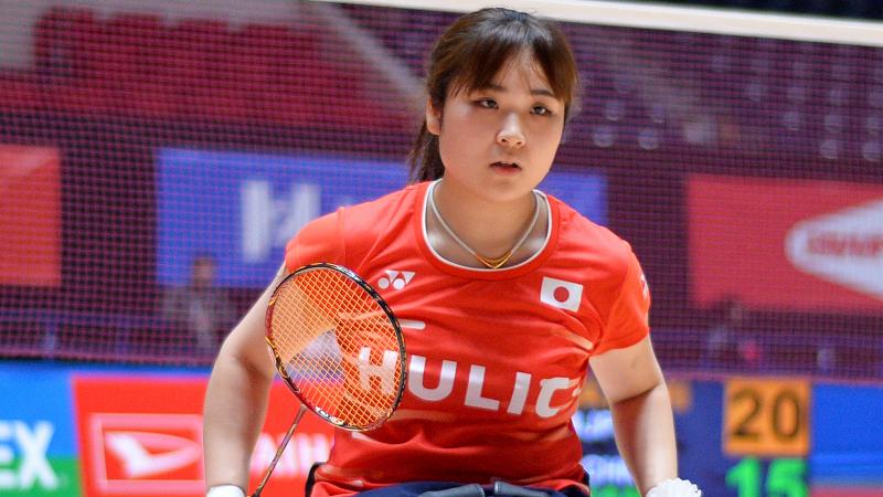 Japanese female athlete in wheelchair holds racket and shuttl