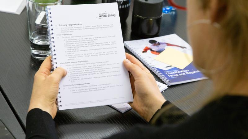 A woman reading a notebook with a World Para Alpine Skiing logo