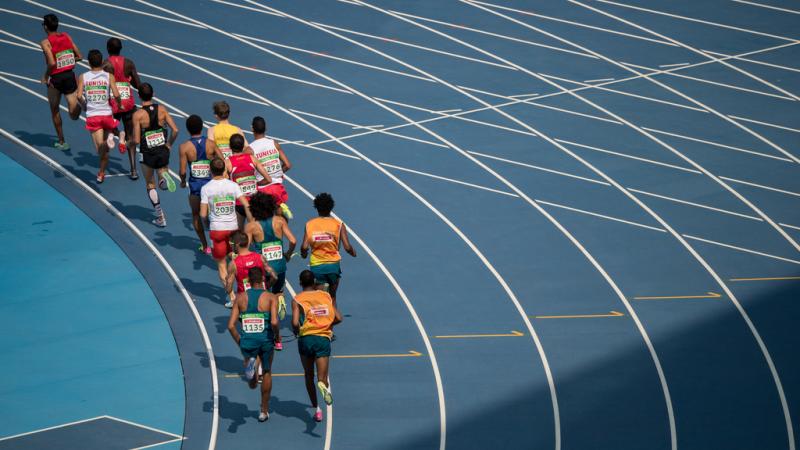 A group of 14 men seen from behind running in a blue athletics track