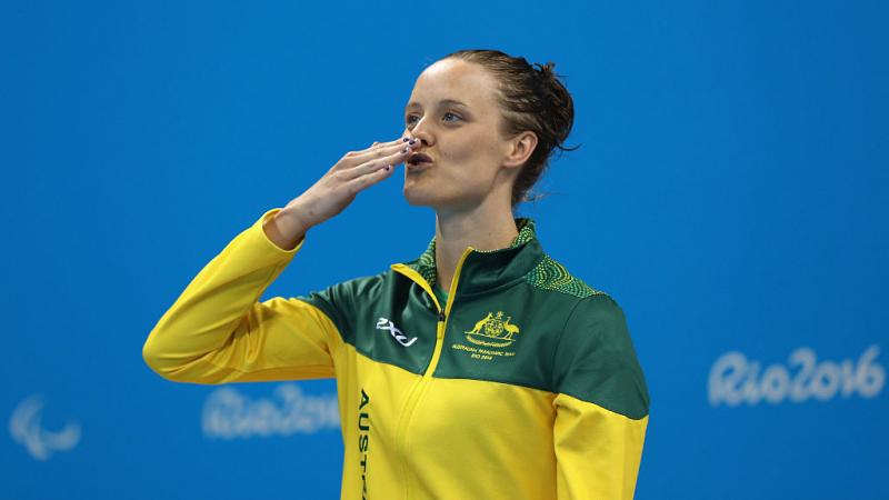 A woman sending a kiss to the audience while standing on the podium waiting to receive a medal