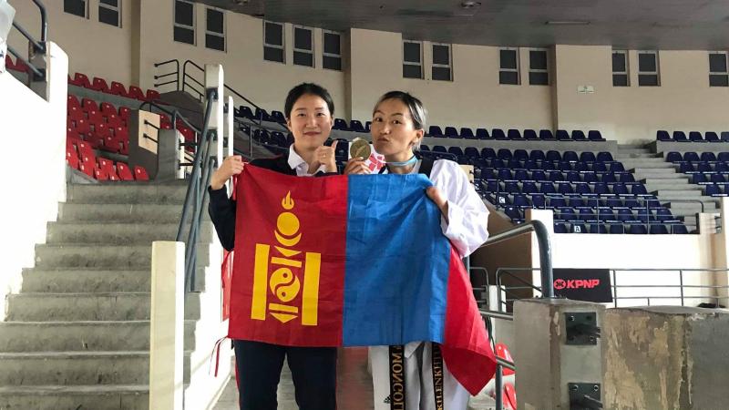 Female taekwondo athlete hold Mongolian flag with friend and her medal