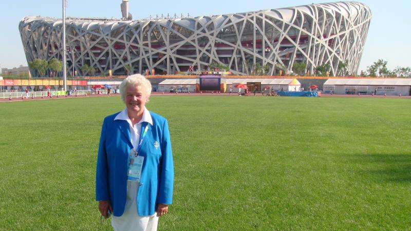 A woman in white skirt and blue jacket posing in front of the athletics stadium during the Beijing 2008 Paralympics
