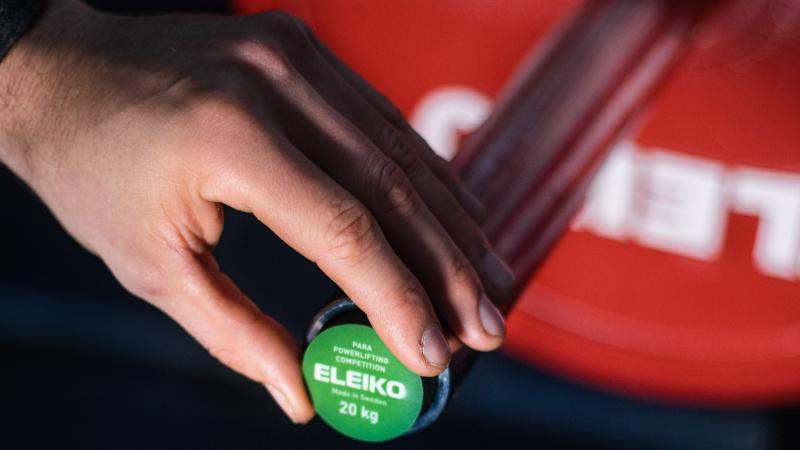 A male hand plugging a green Eleiko sensor on a barbell 