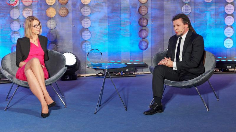 Man and women sit on chairs hosting an awards show