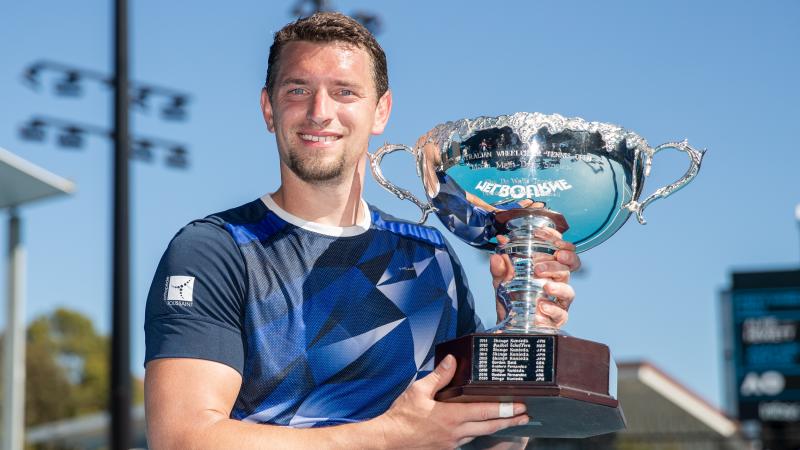 Belgian wheelchair tennis player smiles with Australian Open trophy