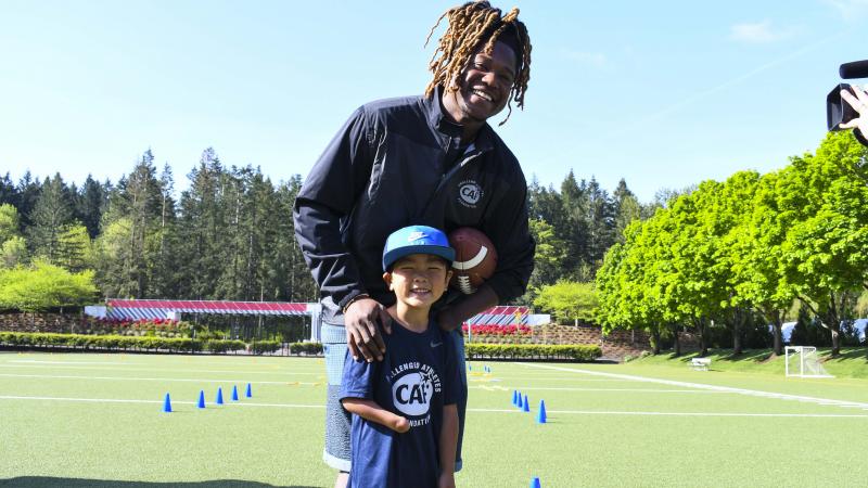 Black male athlete holding an American football and smiling with a kid with an arm impairment
