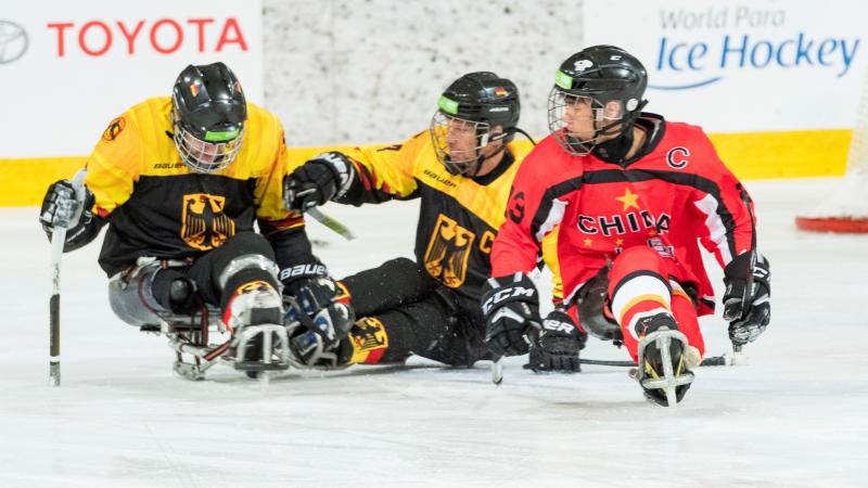 A man with the Chinese uniform on an ice sledge competing against two other men wearing Germany's uniform