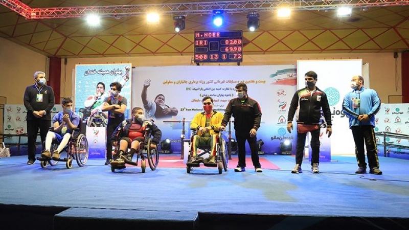 A group of three men in wheelchairs and five standing men on a stage