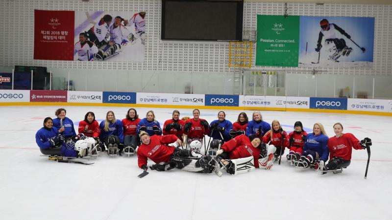 A group of 17 women on sledges wearing read and blue uniforms on an ice rink 