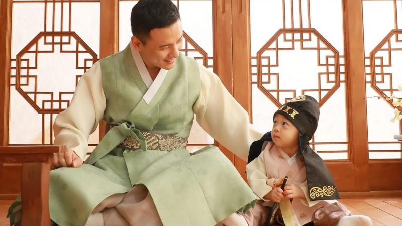 A man in typical Korean clothes looking at a baby on the floor