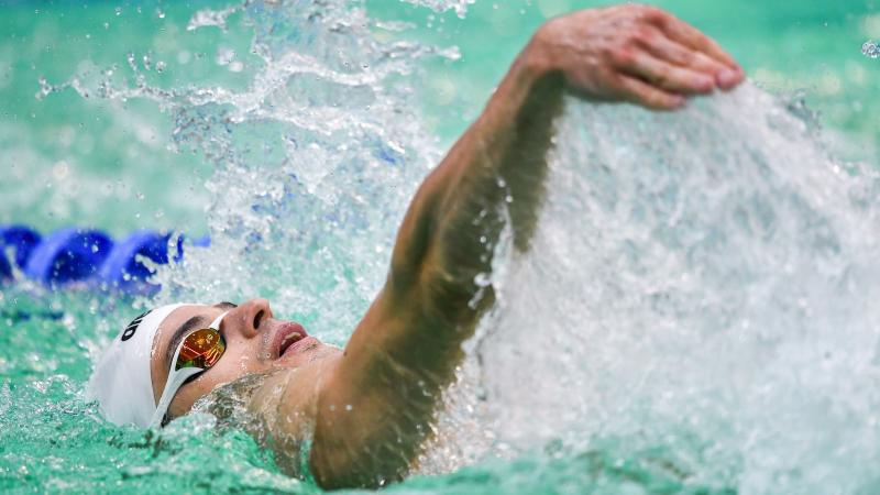 A man with a white cap swimming backstroke in a swimming pool