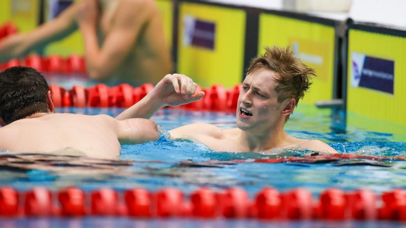 A male swimmer celebrating near another swimmer seeing from behind in a swimming pool