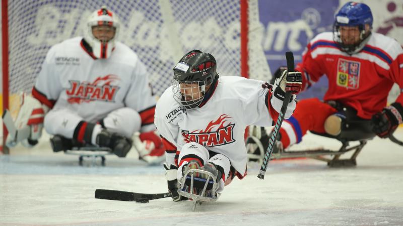 A sledge hockey player from Japan on an ice rink with Japan's goaltender and a Czech Republic player in the background