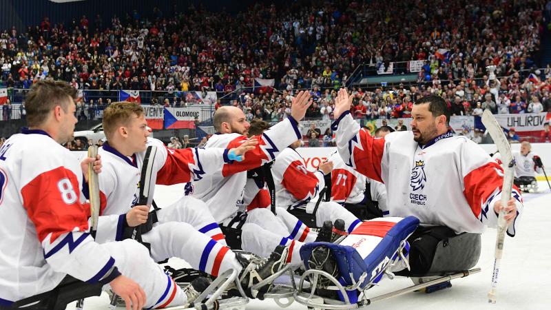 One Para ice hockey player giving high five to a group of players on sledges in a crowded ice hockey arena