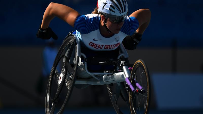 A female athlete competing in a wheelchair race in a blue track