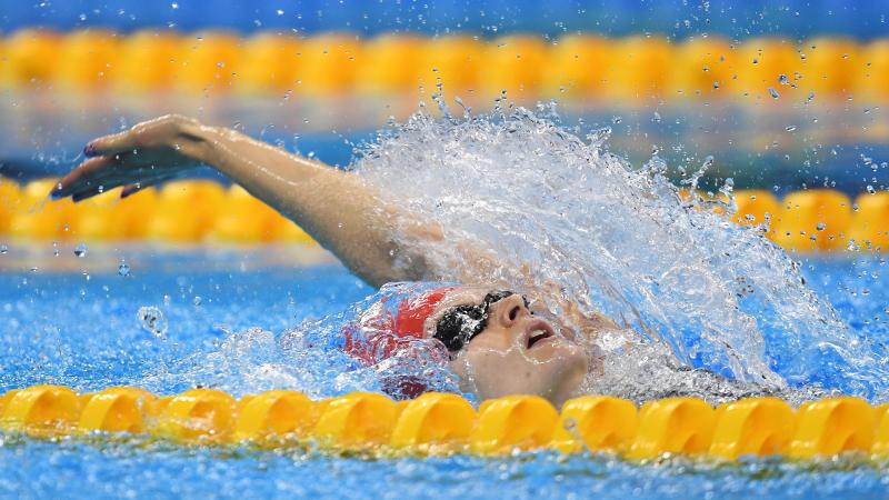 A woman with a red cap swimming backstroke in a pool 