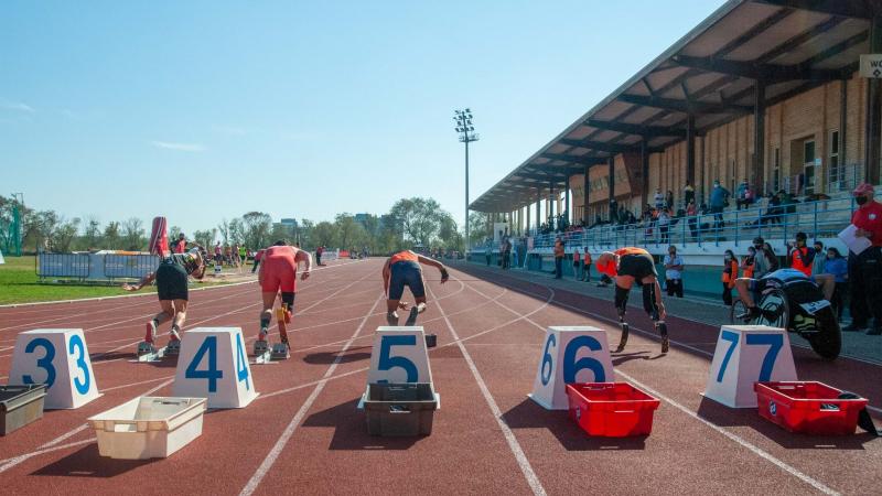 A red athletics track with athletes seeing from behind running from the starting blocks