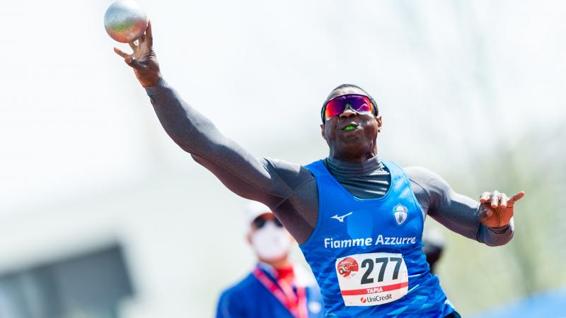 A man competing in shot put observed by another man 