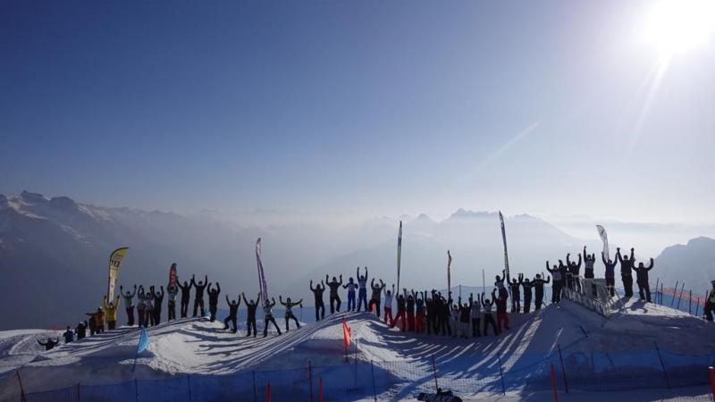 Snowboarders line up along a border-cross slope with their arms raised