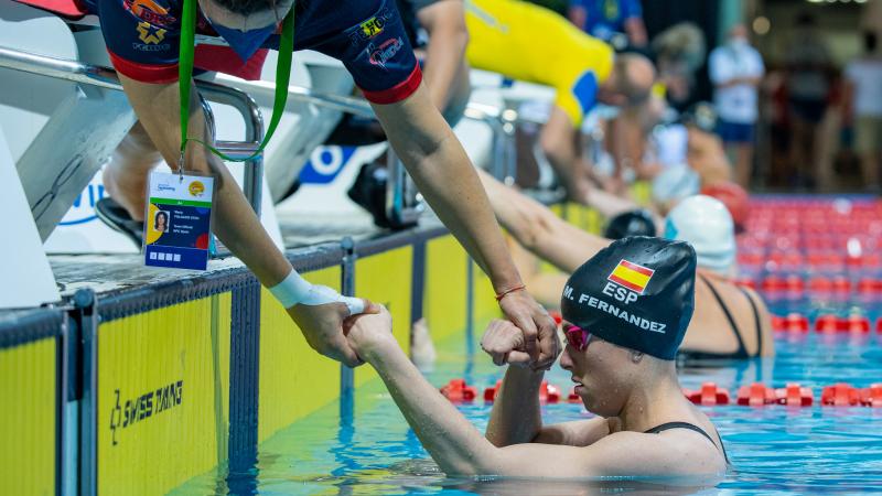 A woman outside a swimming pool grabbing the arms of a female Para swimmer inside the water