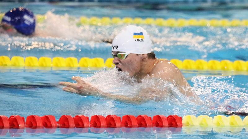 A man with a white cap and the Ukrainian flag swimming breaststroke in a pool