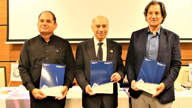 Three men in suits smiling holding a folder