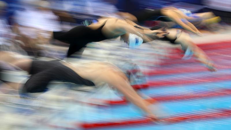 A blurred picture of a group of female swimmers jumping in the pool