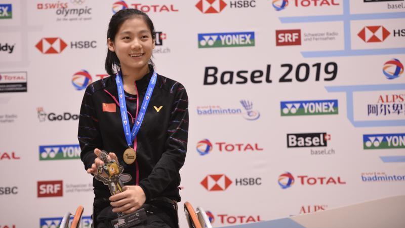 Chinese badminton player Liu Yutong smiles while holding a trophy on the podium