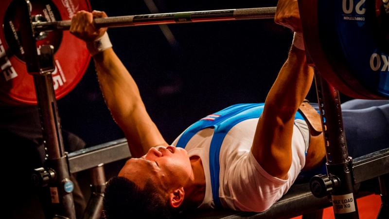 A man on a bench press lifting a bar in a Para powerlifting competition