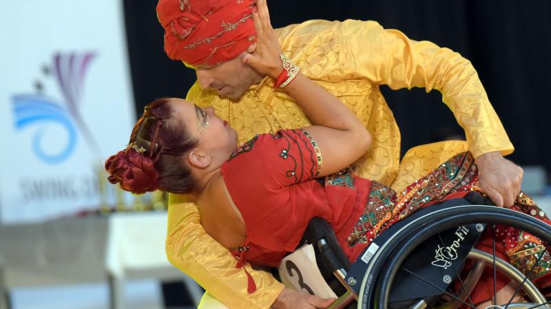 A male standing dancer holding a wheelchair with a female Para dancer during a competition