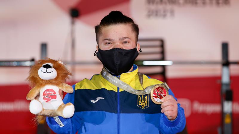 A woman with a face mask showing a medal and a Teddy bear mascot