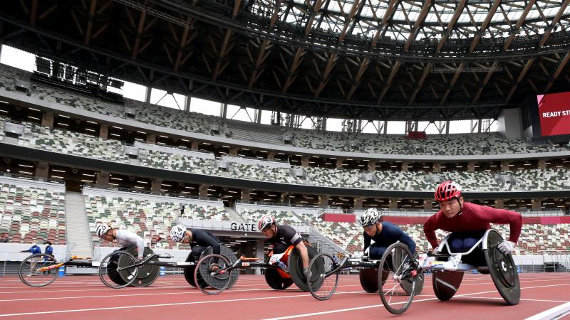 A group of five male wheelchair racers on an athletics track in an empty stadium