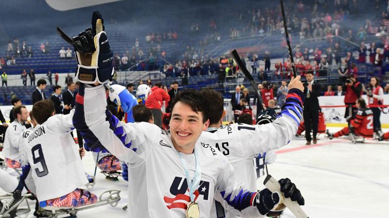 A man celebrating with a group of Para ice hockey players on an ice rink after a match in an indoor arena