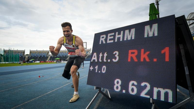 A man with a prosthetic leg celebrating in an athletics track next to a screen showing his world record result