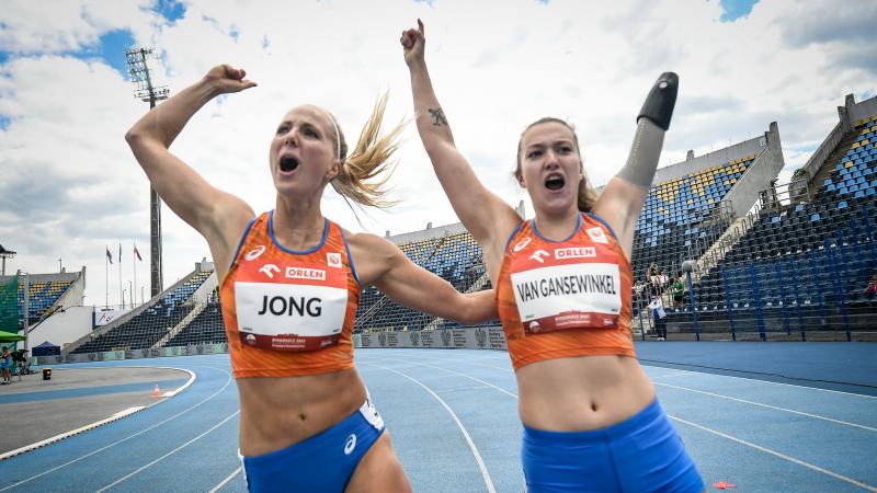 Two women with Netherlands uniform celebrating in a blue athletics track
