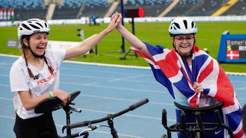 Two young women holding hands on an athletics track