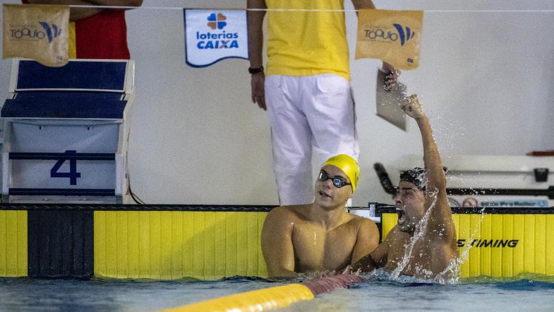 A male swimmer celebrating in the swimming pool next to another male swimmer