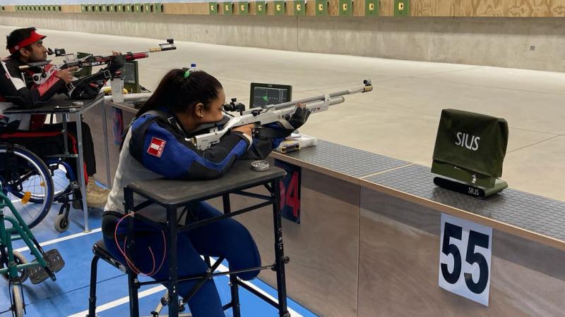 A female leg amputee and a men in a wheelchair practicing shooting in an indoor shooting range