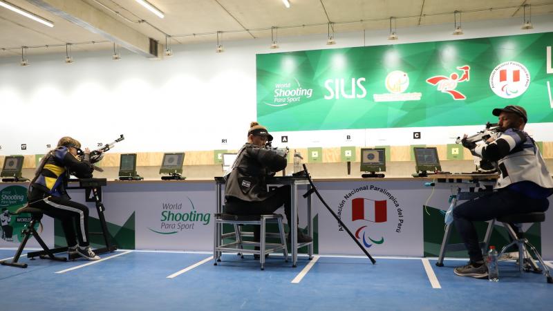 Three persons seated and shooting with rifles in a shooting range