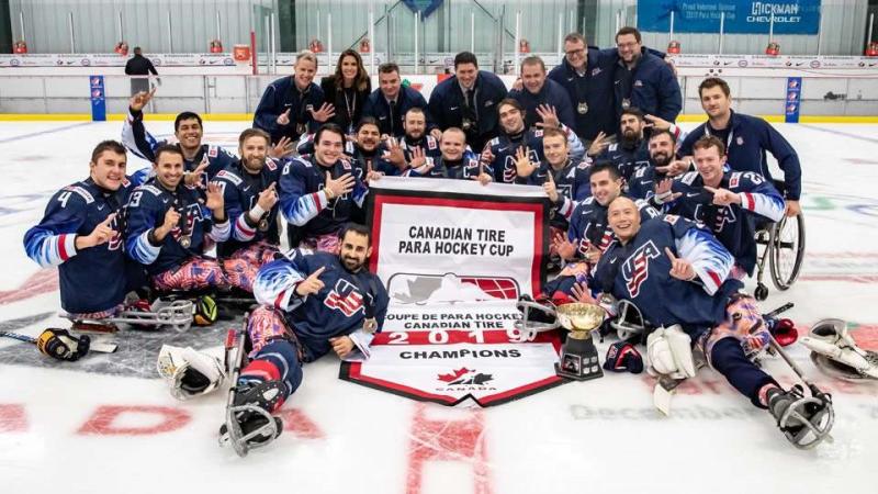 The USA Para ice hockey team posing for picture with a trophy on an ice rink